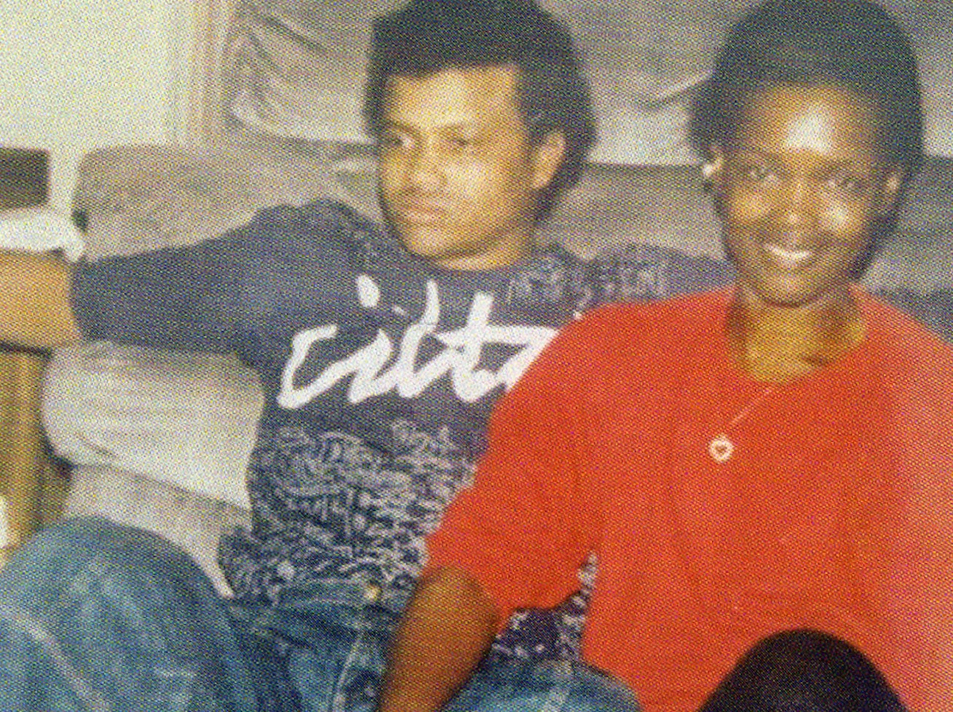 A young Andre Butler sits with a young woman, leaning against a couch.