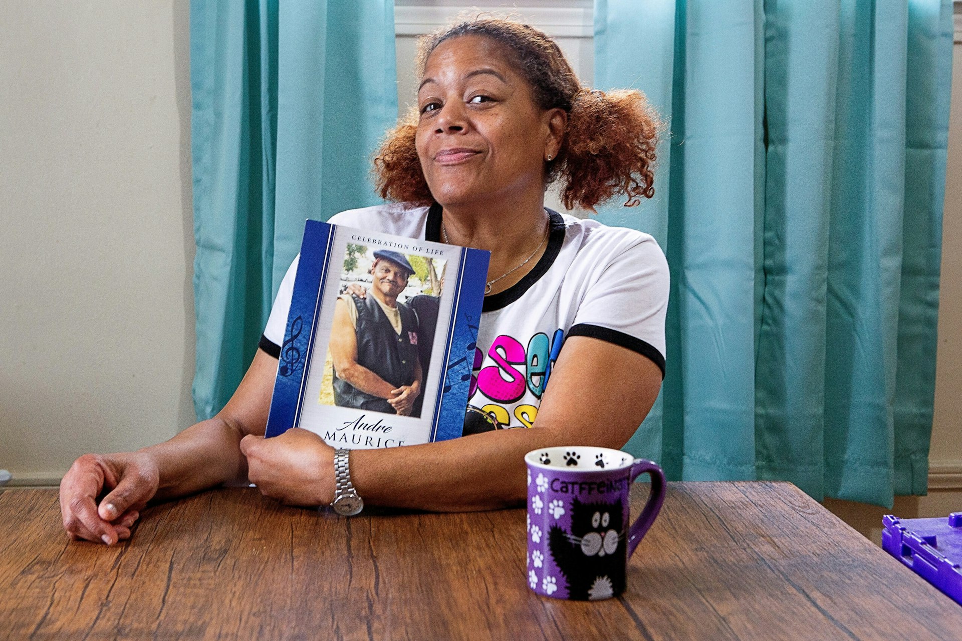 Carla Butler sits at a wooden dining table, holding a picture of her late brother Andre.