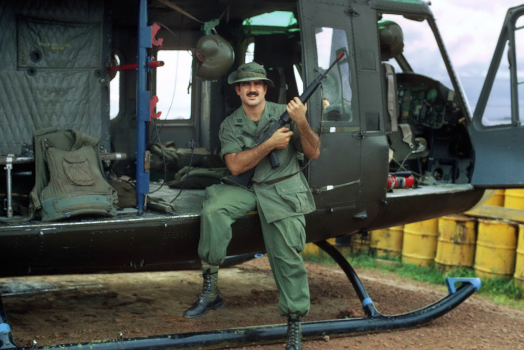 Shad Meshad sits on a helicopter, holding a firearm, in Vietnam.