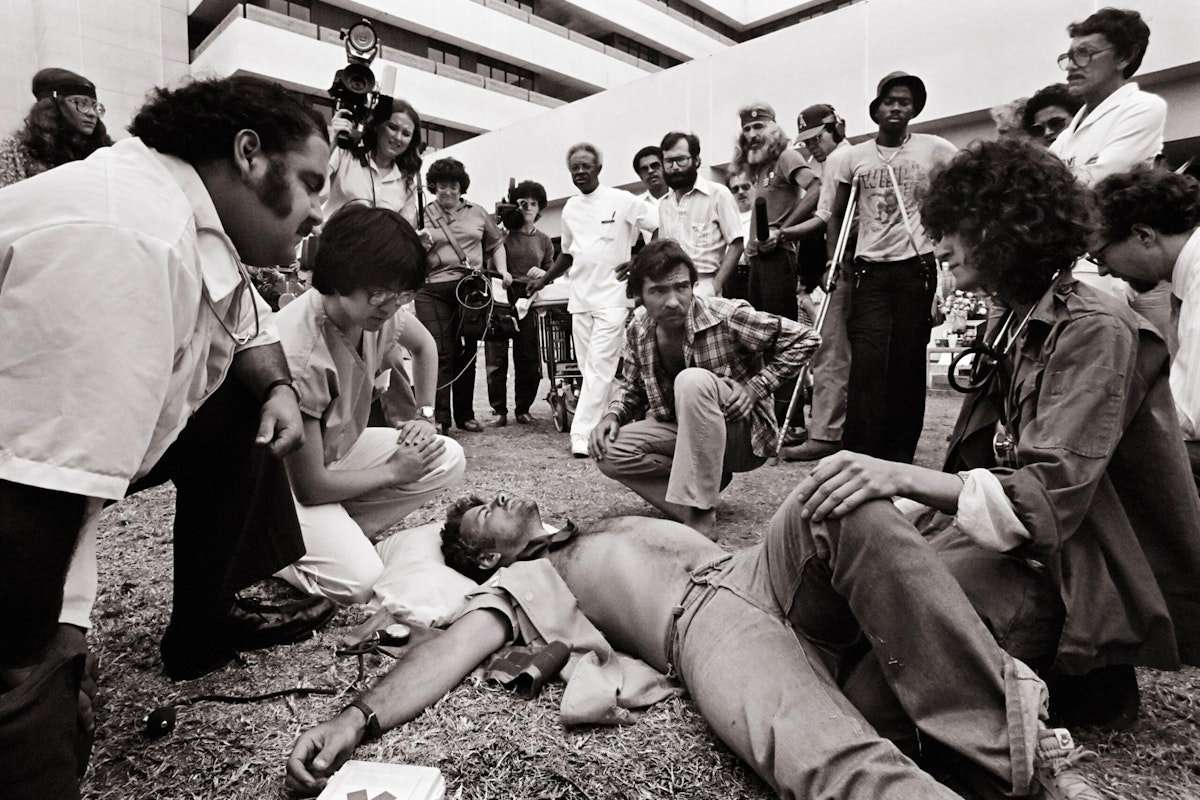 Press and onlookers gather around a collapsed Vietnam veteran at a VA protest, 1981.