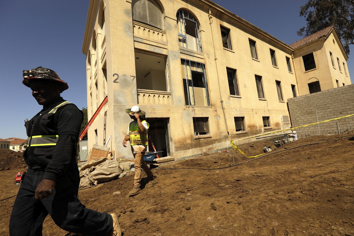 Construction workers walk past Building 207 as it is being refurbished as veterans housing in June 2022.