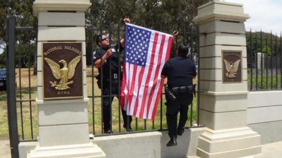 Two VA police officers remove an American flag Rosebrock hung on a VA gate.